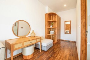 Une salle de bain moderne avec un meuble-lavabo en bois, un miroir rond, un banc gris et une étagère en bois agrémentée de plantes.