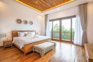 Un dormitorio amplio con una cama grande, suelo de madera y un balcón con cortinas.