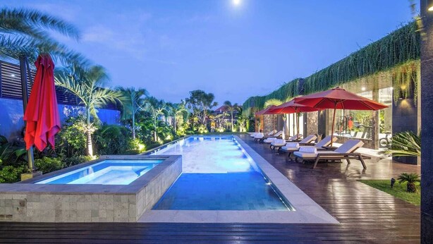 A swimming pool with two separate sections, surrounded by lounge chairs and red umbrellas. - Stylish 5BR Private Villa, Central Seminyak (Seminyak)