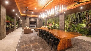 A modern dining area with a long wooden table, black chairs, and a TV. - Stylish 5BR Private Villa, Central Seminyak (Seminyak)