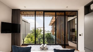 A modern bedroom with a large sliding glass door, a flat-screen TV, and a wooden floor. - Stylish 5BR Beach Villa, 200m in Boho Canggu (Munggu)