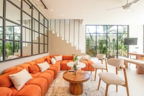 Una sala moderna con un amplio sofá seccional naranja, una mesa de centro redonda de madera y un comedor con una mesa y sillas de madera.