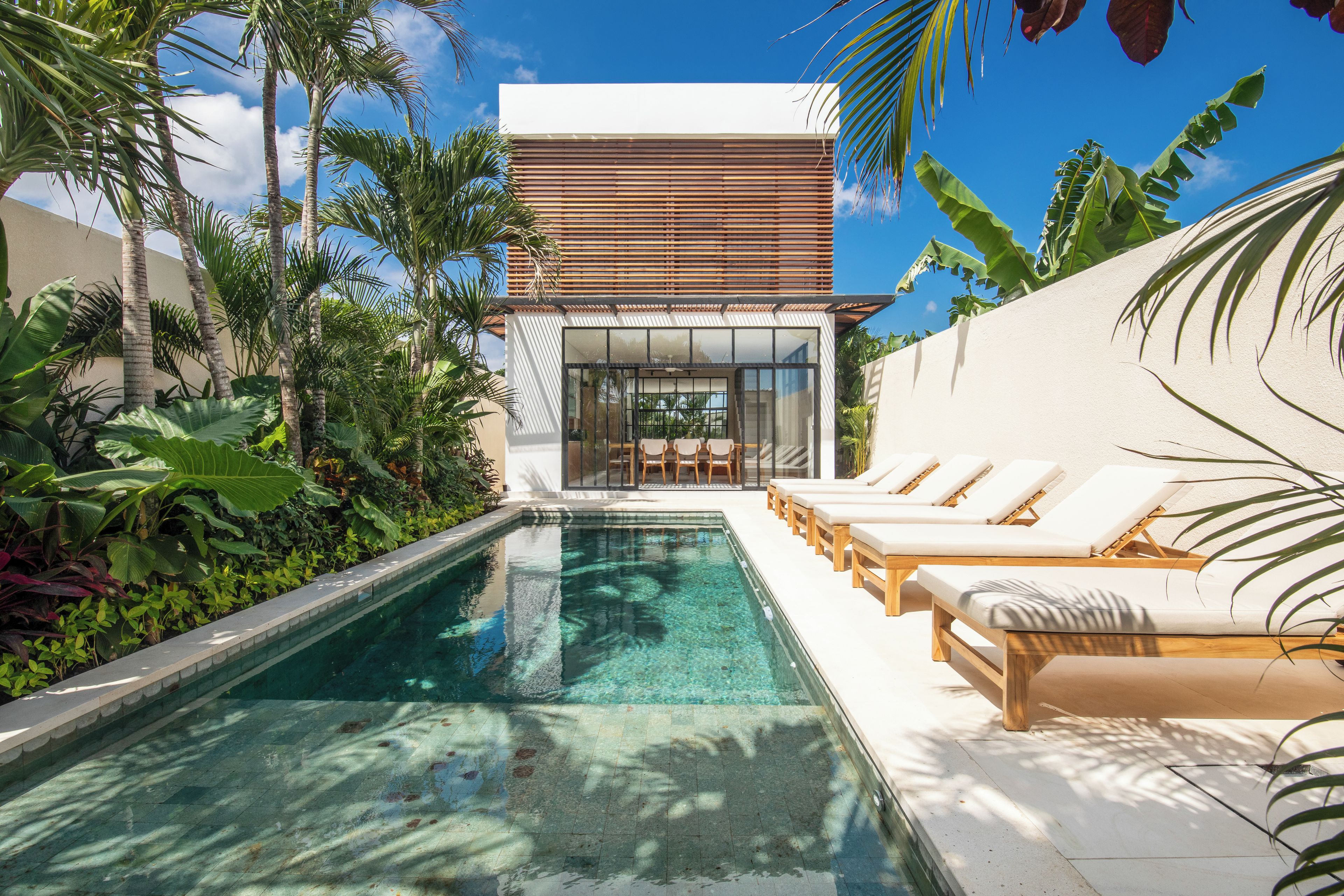A modern pool area with lounge chairs and a clear pool, surrounded by tropical plants.