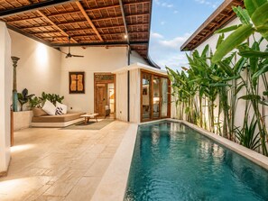 Un área de piscina interior moderna con un ventilador de techo, un sofá y una puerta que da a otra habitación.
