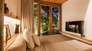 Una habitación con sofá, televisión, techo de madera y vistas a una piscina y plantas.