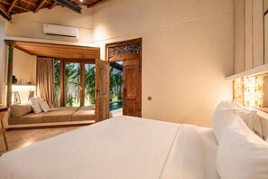 A bedroom with a large bed, a wooden door, and a view of greenery outside.