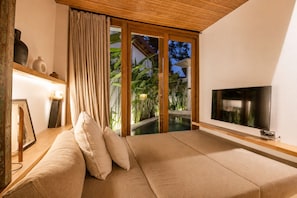 Una habitación con sofá, televisión, techo de madera y vistas a una piscina y plantas.
