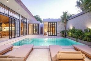 Un’area piscina moderna con sedie a sdraio, una piscina e vista sugli spazi interni.
