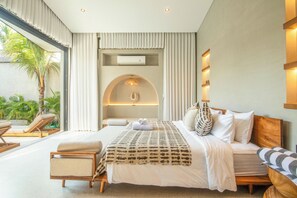 A modern hotel room with a large bed, a seating area with a sofa and chairs, and a view of palm trees outside. - Luxurious 5BR Boho Sanctuary, Near Bingin Beach (Pecatu)