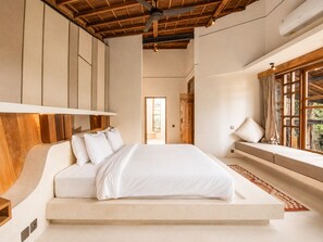 Un dormitorio moderno con una cama grande, cabecera de madera y vista a la vegetación a través de una ventana.