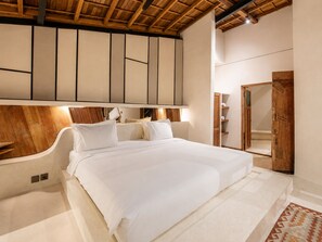 A bedroom with a large bed, wooden ceiling beams, a wardrobe, and a mirror.
