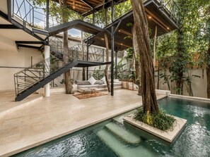 Un espace piscine intérieur moderne, doté d’un escalier, de sièges et d’un arbre.