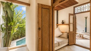 A room with a wooden door, a cushioned seating area, a small table, and a view of a pool. - Serene 1BR Villa 800 to Echo Beach, With Pool (Canggu)