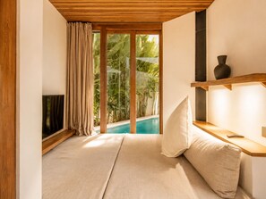 Quarto moderno com cama, televisão, prateleira de madeira e vista para uma piscina.