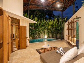 A poolside area with a wooden door, a pool, a small table, and a sofa with pillows. - Lush 1-br Villa With Pool, 4 Mins to Echo Beach, (Canggu)