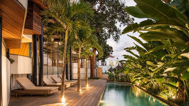 Un espace aménagé au bord de la piscine, avec des chaises longues, une terrasse en bois et des plantes tropicales.