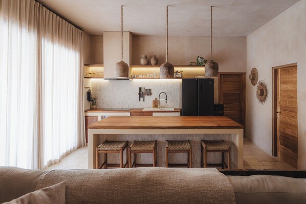A modern kitchen with a central island, bar stools, hanging pendant lights, and wooden cabinetry.