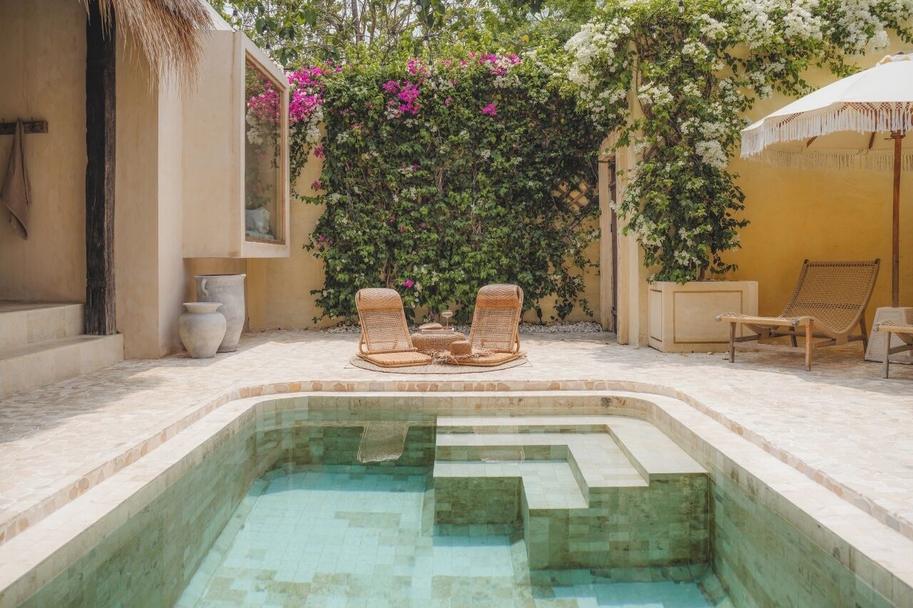 Un espace piscine agrémenté de chaises longues et d’une petite table, le tout entouré d’une végétation luxuriante et de fleurs.