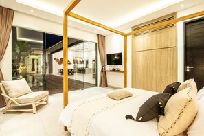 A modern bedroom with a large bed, a glass partition, a dining area, and a TV. - Modern 4 BR Villa 400m to the Beach in Canggu (Canggu)
