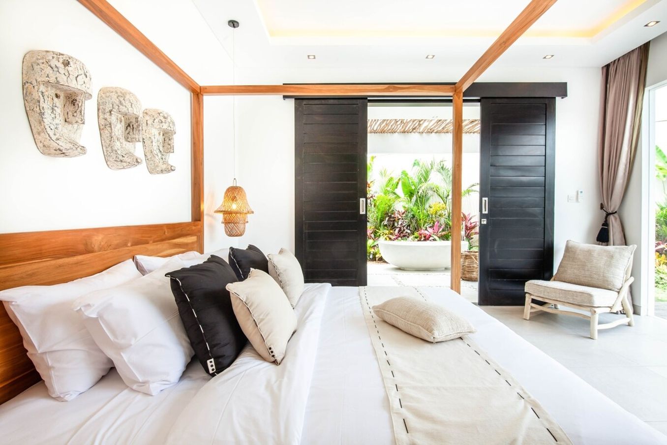 A modern bedroom with a large bed, a wooden headboard, and a view of a garden through an open door.