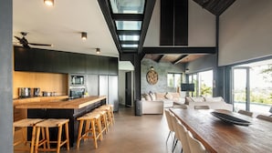 A modern kitchen with a central island, bar stools, and a dining area with a long table and chairs. - Elegant 6BR Clifftop Villa Near Bingin (Pecatu)