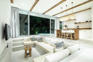 A modern living room with a large sectional sofa, a wooden coffee table, and a kitchen area with a dining table and bar stools.
