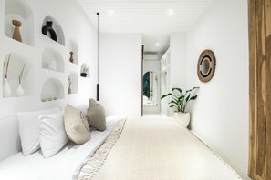 Een moderne slaapkamer met een bed, kussens, een kamerplantje en een gang naar een andere kamer.