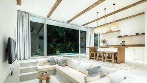 A modern living room with a large sectional sofa, a wooden coffee table, and a kitchen area with a dining table and bar stools. - Chic 2BR Villa, 5min to Bingin's Coastal Bliss (Pecatu)