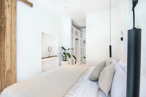 A bedroom with a large bed, a wooden door, a white wall, and a plant.