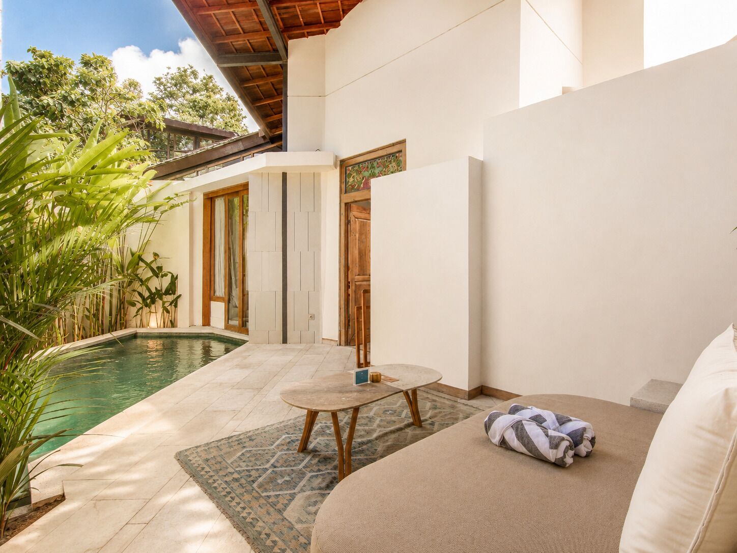 Zona piscina con un divano, un tavolo e una porta che dà su un portico coperto.