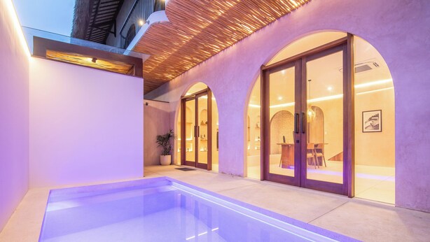 Un espace piscine intérieur moderne, doté d’une piscine à eau claire, de portes vitrées donnant sur une pièce et d’un éclairage d’ambiance chaleureux.