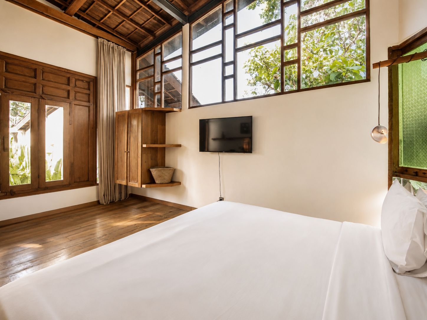 Un dormitorio con una cama grande, vigas de madera, un televisor y una ventana con vistas a zonas verdes.