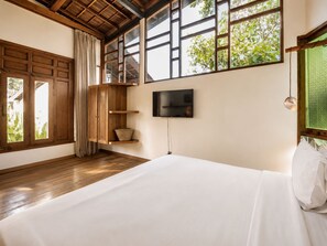 A bedroom with a large bed, wooden beams, a TV, and a window with a view of greenery. - Luxurious 1-br Villa With Pool, Echo Beach 800m (Canggu)