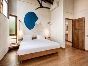 Ein Schlafzimmer mit einem hölzernen Bett, einer großen, blau-weißen abstrakten Wandkunst, einem Deckenventilator und einer Holztür.
