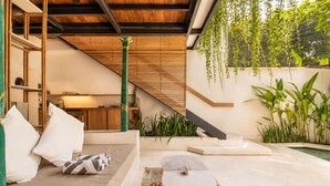 A modern outdoor living area with a sofa, a patterned rug, a small table, and a staircase leading to a kitchen. - Luxurious 1-br Villa With Pool, Echo Beach 800m (Canggu)