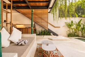 Un espace de vie extérieur moderne comprenant un canapé, un tapis à motifs, une petite table et un escalier menant à la cuisine.