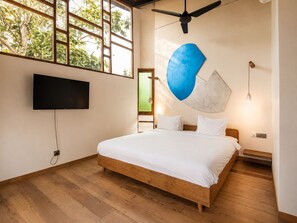 Une chambre à coucher avec un lit, une télévision, un ventilateur de plafond et une fenêtre donnant sur des arbres.