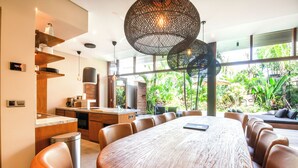 A modern kitchen with a large island, a dining area with a round table and chairs, and large windows offering a view of greenery. - Luxury 6BR Canggu 400m to Finns Beach (Canggu)