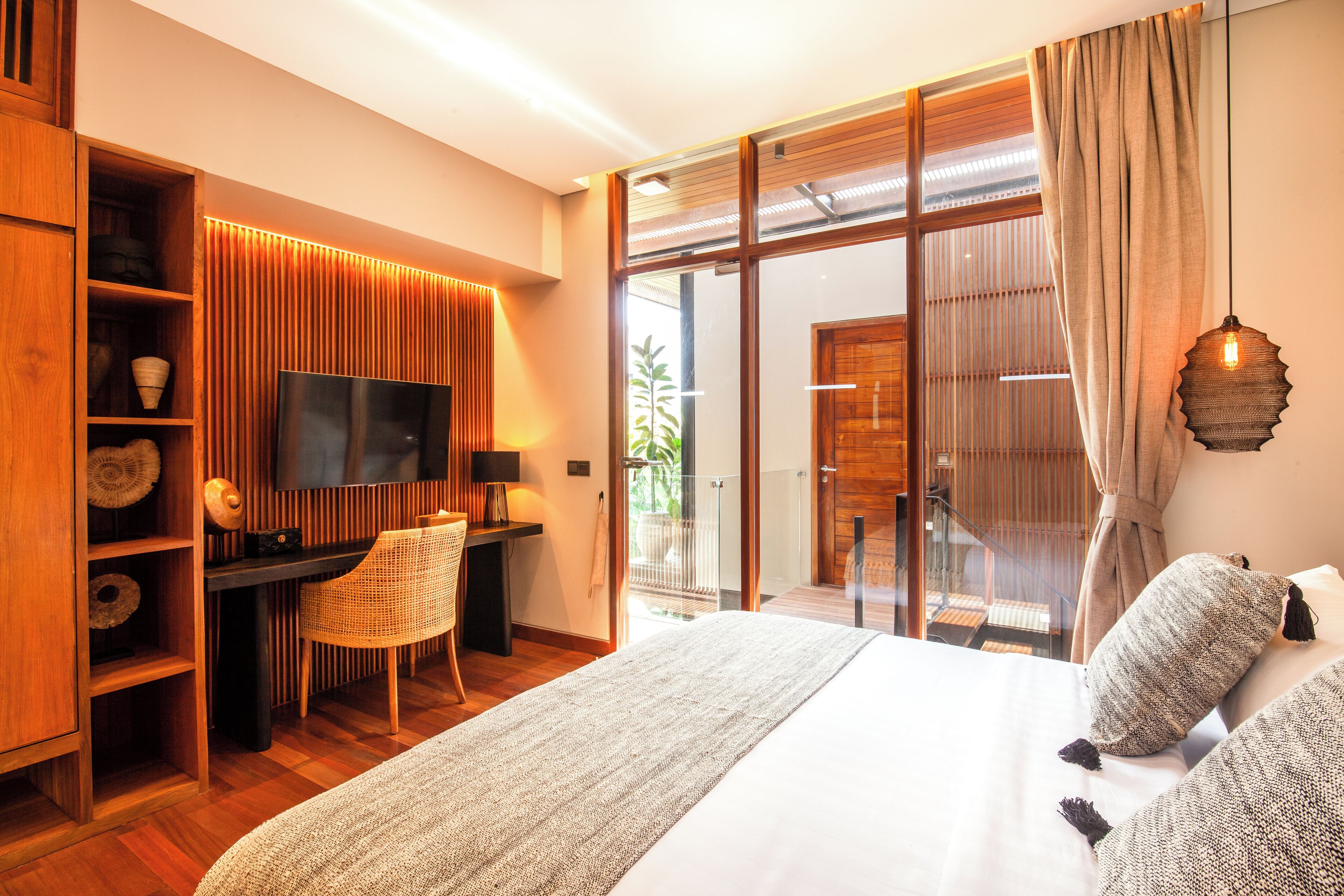 A modern hotel room with a large bed, a desk with a chair, a television, and a balcony with a view.
