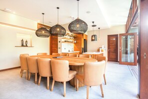 A modern dining area with a round wooden table, beige chairs, and pendant lighting. - Luxury 6BR Canggu 400m to Finns Beach (Canggu)