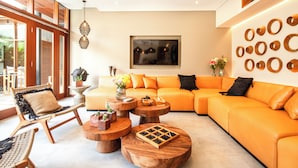 A modern living room with a large orange sectional sofa, wooden coffee tables, and a wicker chair. - Luxury 6BR Canggu 400m to Finns Beach (Canggu)