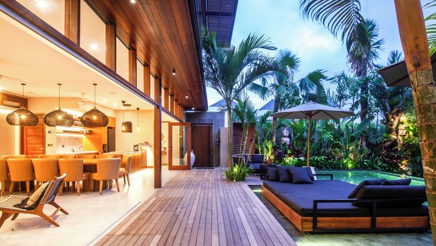 A wooden deck with a dining area, a pool, and a lounge with a view of the surrounding greenery. - Luxury 6BR Canggu 400m to Finns Beach (Canggu)