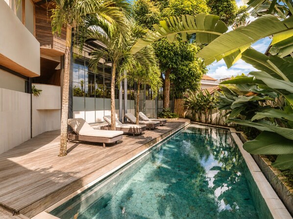 A swimming pool with lounge chairs, surrounded by tropical plants and a modern building.