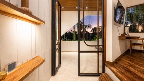 A modern interior with a wooden bench, a TV, and a view of a sunset through a glass door. - Modern 1-br Loft With Art Deco Style Shared Pool (Canggu)