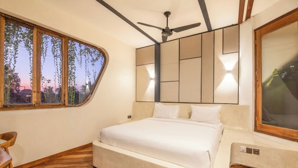 A bedroom with a bed, a ceiling fan, a large window, and a view of trees. - Modern 1-br Loft With Art Deco Style Shared Pool (Canggu)