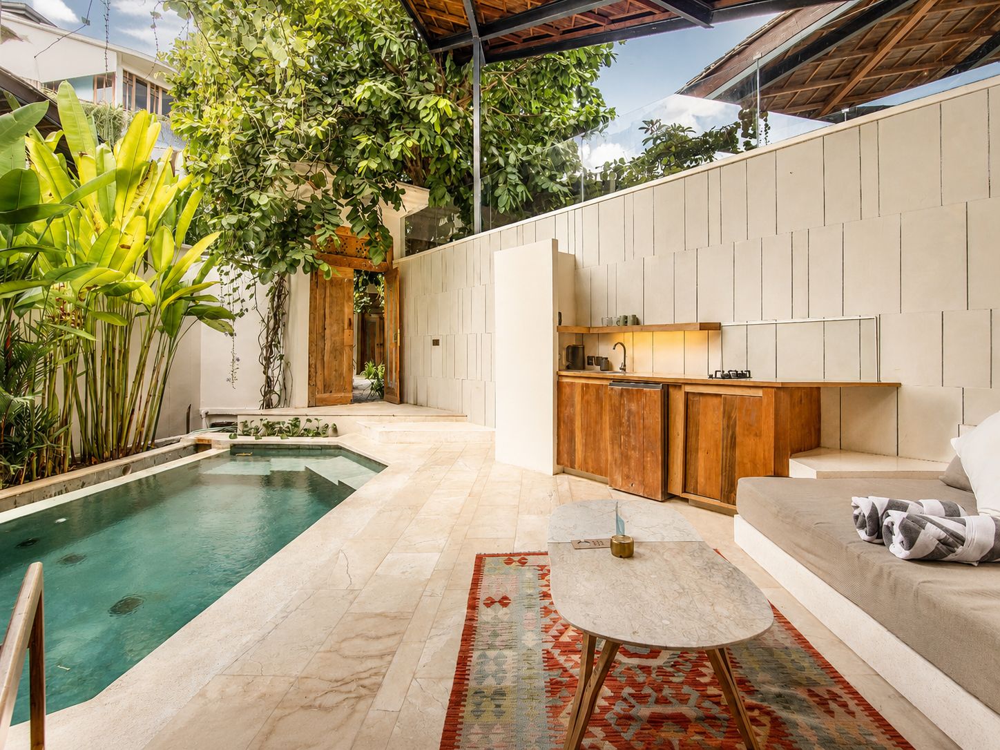 A modern outdoor living space with a pool, wooden furniture, and a kitchen area.