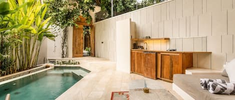 A modern outdoor living space with a pool, wooden furniture, and a kitchen area.