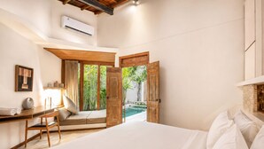 A bedroom with a large bed, a desk, and a view of an outdoor pool. - Chic 1-br Villa With Pool, 4 Mins to Echo Beach (Canggu)