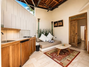 A compact living space with a kitchenette, a sofa, a small round table, and a patterned rug. - Stunning 1-br Villa With Pool, Echo Beach 4mins (Canggu)