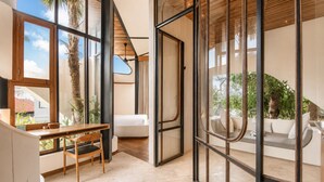 A modern interior with a dining area, a sofa, and a view of greenery outside. - Modern 1-br Loft With Art Deco Style and Shared Po (Canggu)
